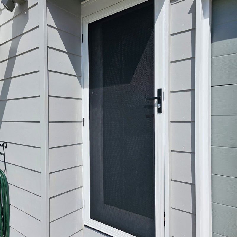 White hinged security screen door on a weatherboard home entry