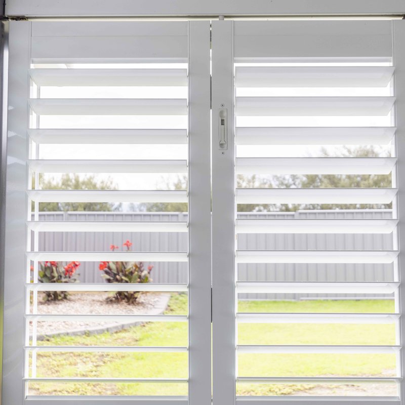 Pair of white aluminium shutter doors with the blades open to the garden