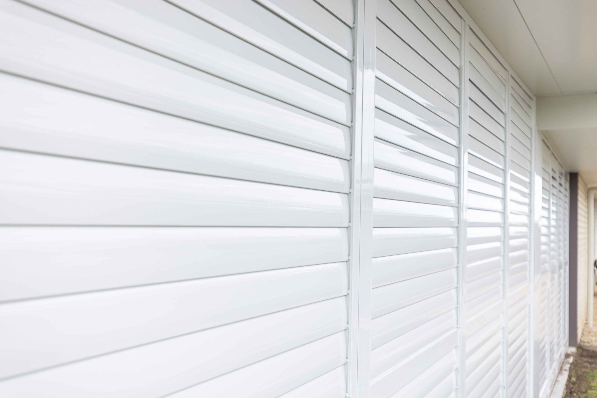 Long run of closed white aluminium shutters inside a patio enclosure