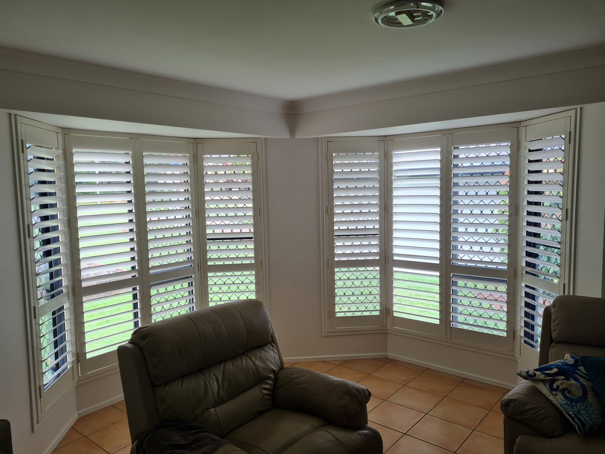 White plantation shutters on a living room bay window beside a recliner