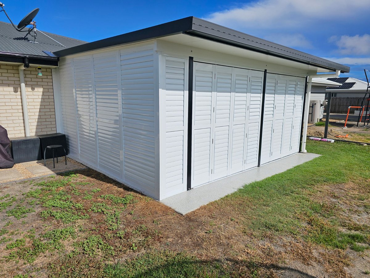 Alfresco area fully enclosed in white aluminium shutters, seen from the lawn under a blue sky