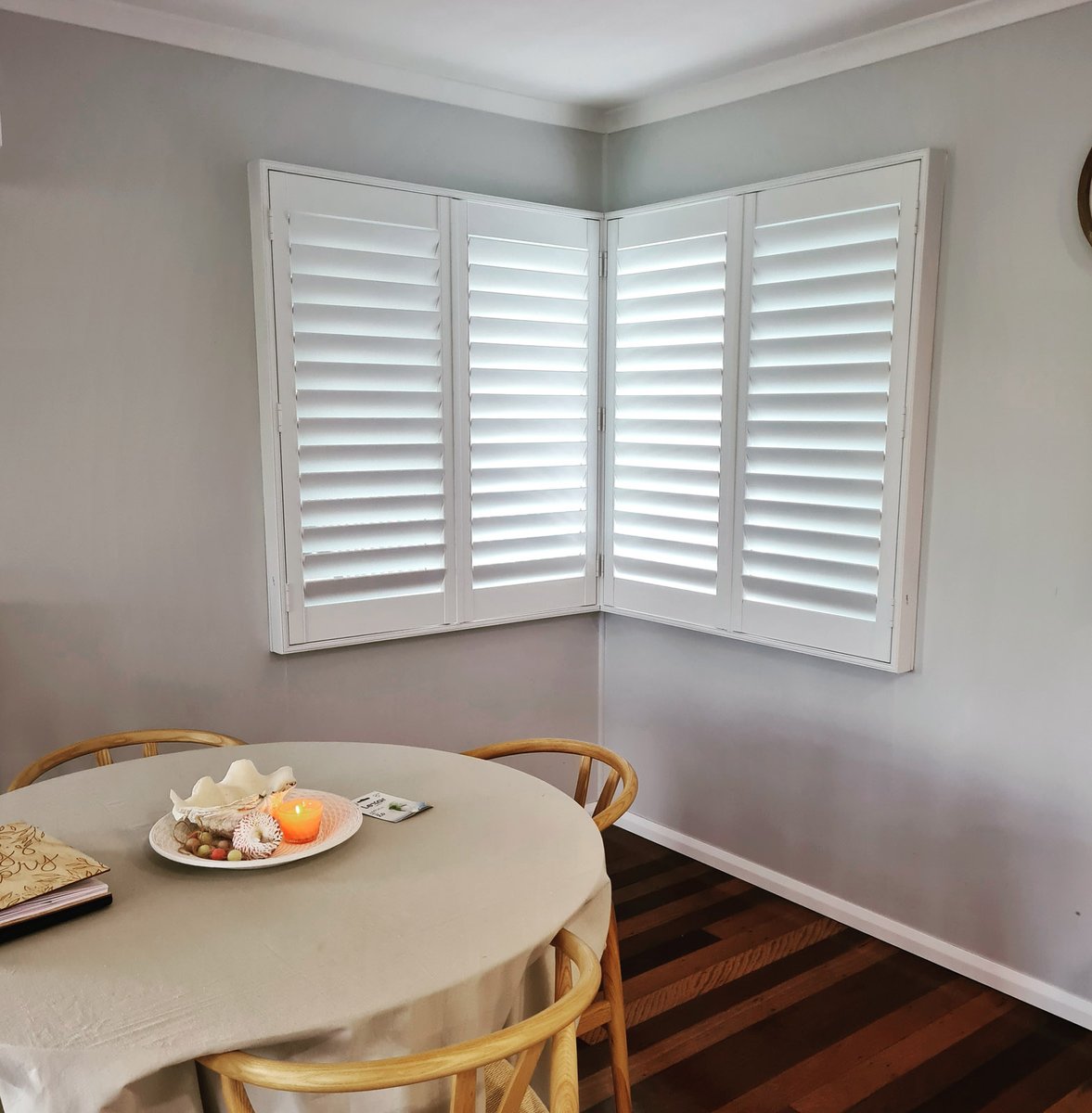 White plantation shutters on a corner window above a dining table